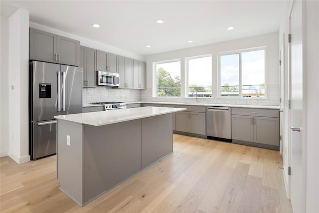 kitchen with a center island, light hardwood / wood-style flooring, gray cabinets, appliances with stainless steel finishes, and tasteful backsplash