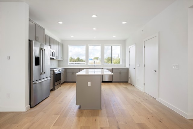 kitchen with gray cabinetry, backsplash, light wood-type flooring, a kitchen island, and stainless steel appliances