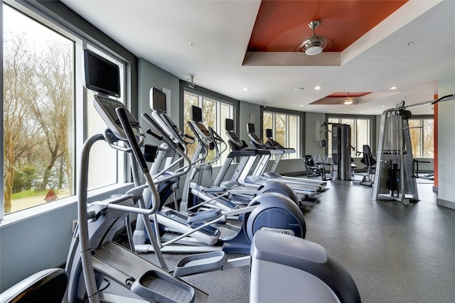 gym with a tray ceiling, a wealth of natural light, and ceiling fan