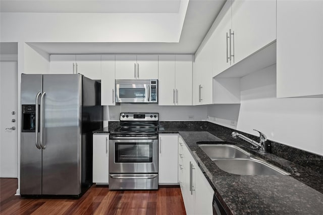 54 Rainey St Unit 613, Austin, TX 78701 - kitchen featuring stainless steel appliances, a sink, dark wood-style flooring, white cabinetry, and dark stone countertops