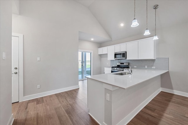 kitchen featuring high vaulted ceiling, white cabinets, hardwood / wood-style flooring, appliances with stainless steel finishes, and kitchen peninsula