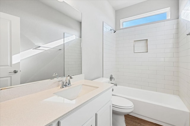 full bathroom with hardwood / wood-style floors, vanity, tiled shower / bath combo, and toilet