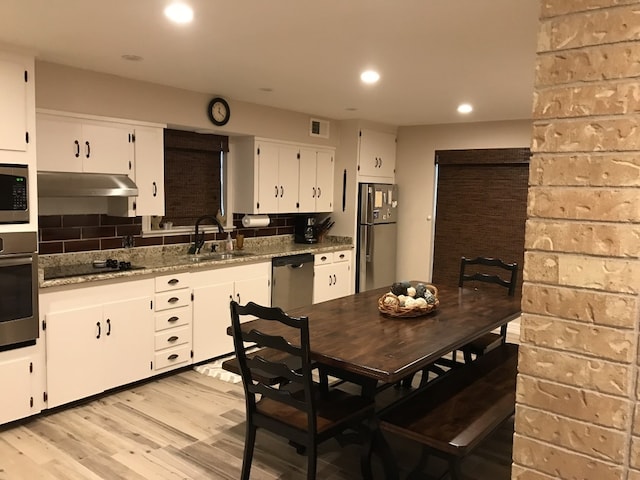 kitchen with light stone countertops, appliances with stainless steel finishes, sink, white cabinets, and light hardwood / wood-style floors