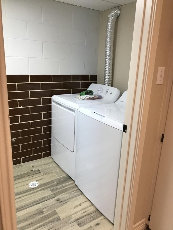 laundry area with washer and dryer, tile walls, and light wood-type flooring