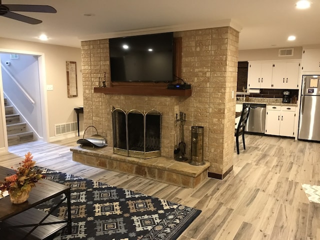 living room with ceiling fan, light hardwood / wood-style floors, and a brick fireplace