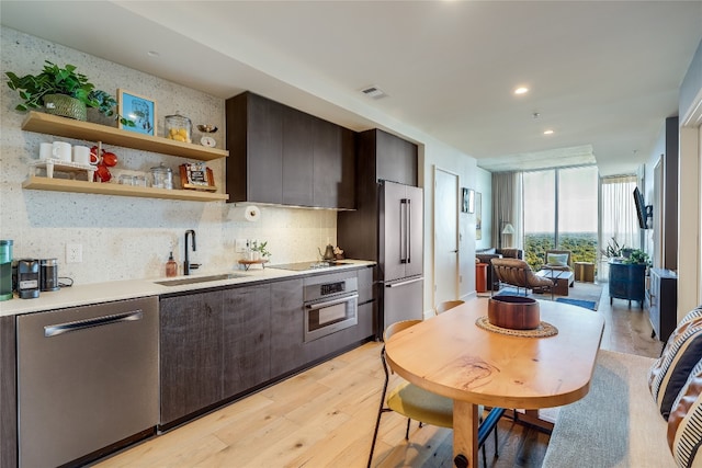 kitchen with sink, decorative backsplash, dark brown cabinets, light hardwood / wood-style floors, and stainless steel appliances