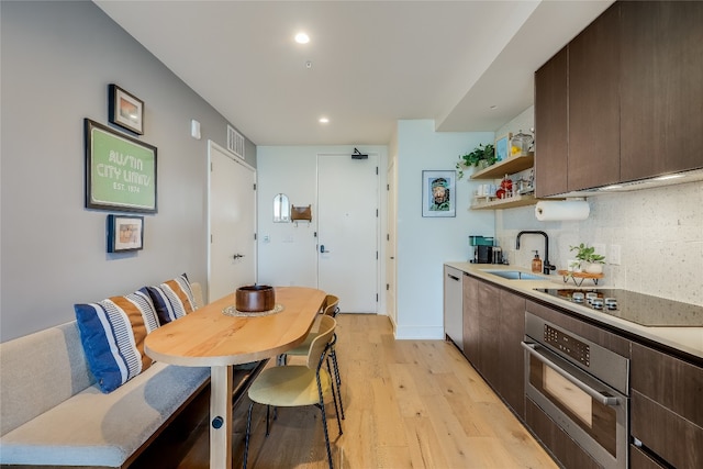 kitchen with stainless steel oven, sink, light wood-type flooring, black electric cooktop, and dark brown cabinets