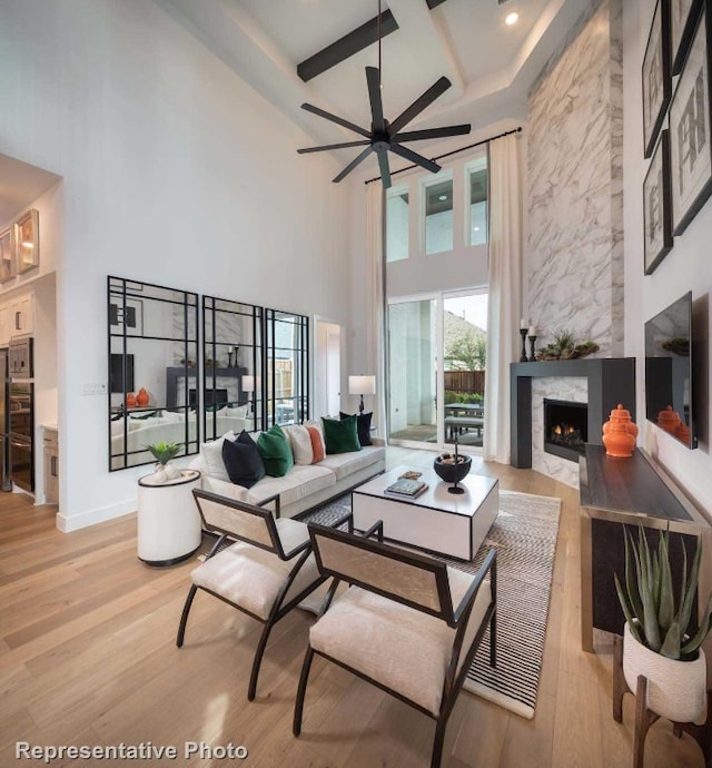 living room featuring ceiling fan, a fireplace, a high ceiling, and light hardwood / wood-style flooring