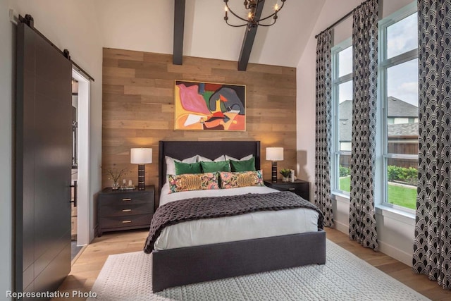 bedroom with light wood-type flooring, a barn door, multiple windows, and wooden walls