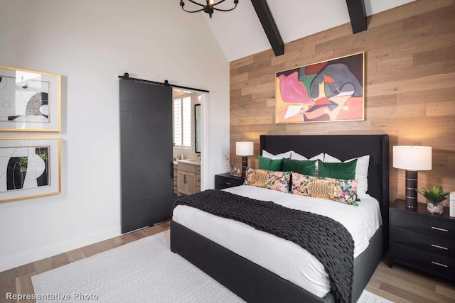 bedroom featuring wood walls, light hardwood / wood-style flooring, a barn door, connected bathroom, and beam ceiling