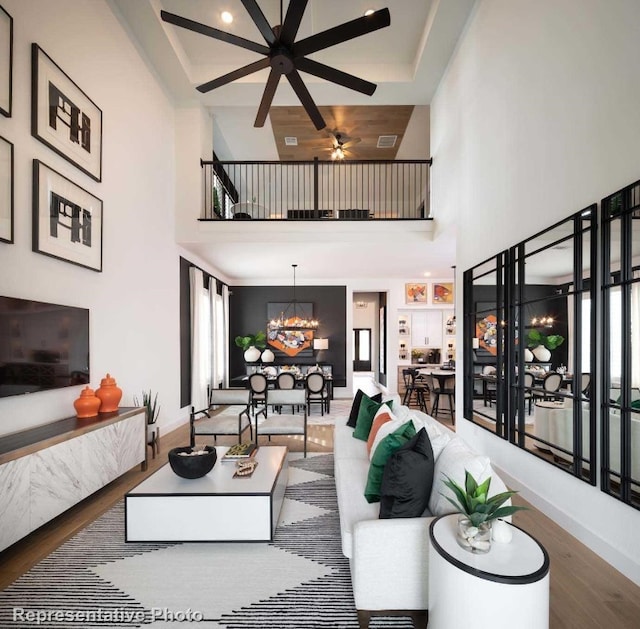 living room featuring ceiling fan with notable chandelier, wood-type flooring, and a high ceiling