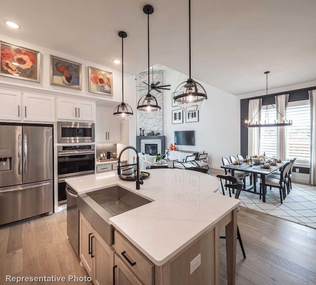 kitchen featuring hanging light fixtures, stainless steel appliances, light hardwood / wood-style floors, a center island with sink, and white cabinets