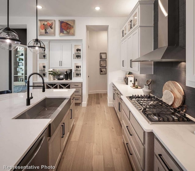 kitchen featuring stainless steel appliances, white cabinets, wall chimney exhaust hood, and hanging light fixtures