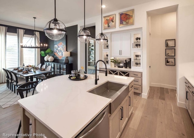 kitchen featuring sink, hanging light fixtures, stainless steel dishwasher, light hardwood / wood-style floors, and a center island with sink