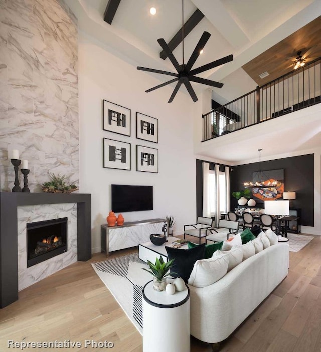 living room with beam ceiling, a premium fireplace, wood-type flooring, and ceiling fan with notable chandelier