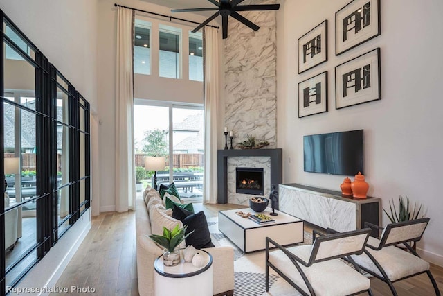 living room featuring ceiling fan, light wood-type flooring, a fireplace, and a towering ceiling