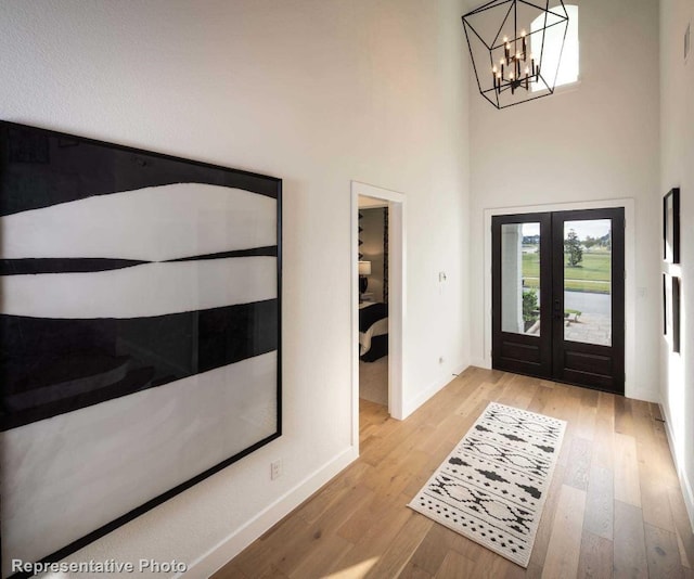 entryway with a chandelier, french doors, a towering ceiling, and light hardwood / wood-style floors