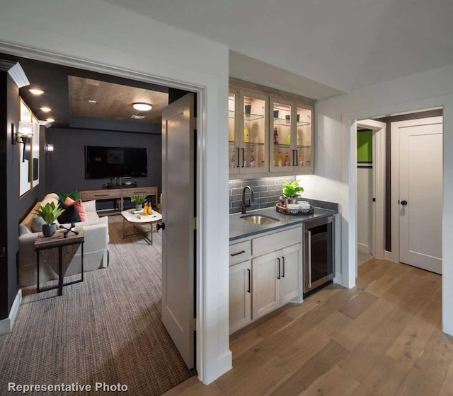 bar with sink, beverage cooler, light hardwood / wood-style floors, decorative backsplash, and white cabinets