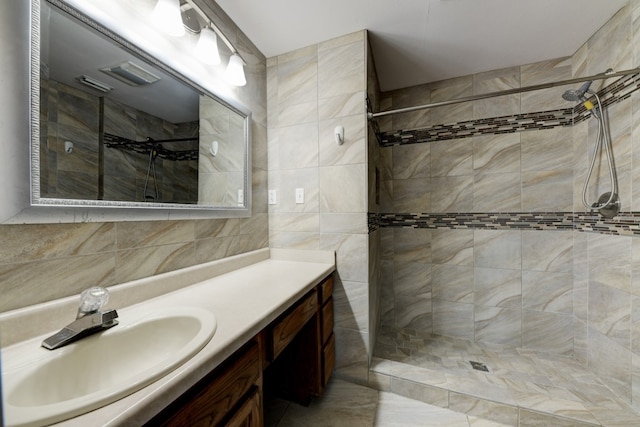 bathroom featuring vanity, a tile shower, and tile walls