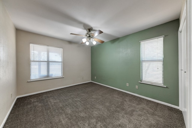 spare room with ceiling fan, plenty of natural light, and dark colored carpet