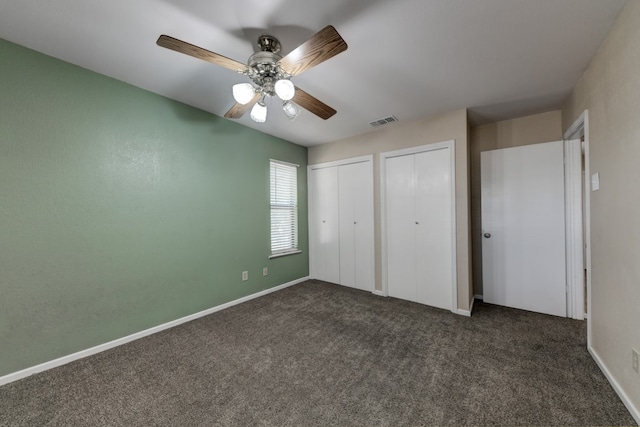 unfurnished bedroom with dark colored carpet, ceiling fan, and two closets