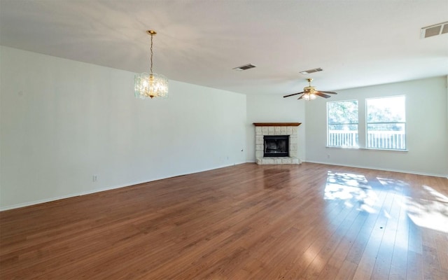 unfurnished living room featuring a fireplace, wood-type flooring, and ceiling fan with notable chandelier