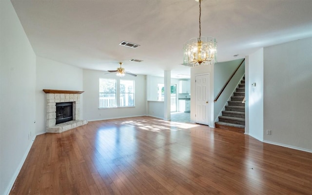 unfurnished living room featuring ceiling fan with notable chandelier, hardwood / wood-style flooring, and a stone fireplace