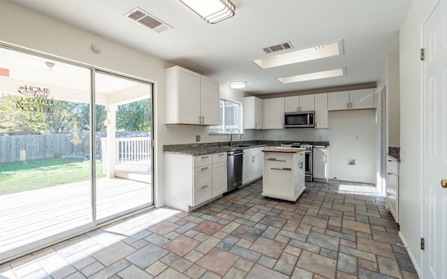 kitchen with dark stone counters, stainless steel appliances, a kitchen island, sink, and white cabinetry