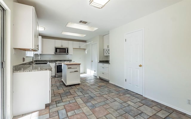 kitchen with a center island, sink, light stone counters, white cabinetry, and stainless steel appliances