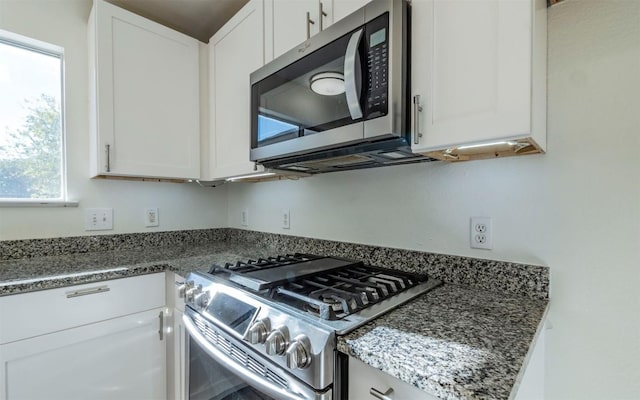 kitchen with appliances with stainless steel finishes, white cabinetry, and dark stone counters