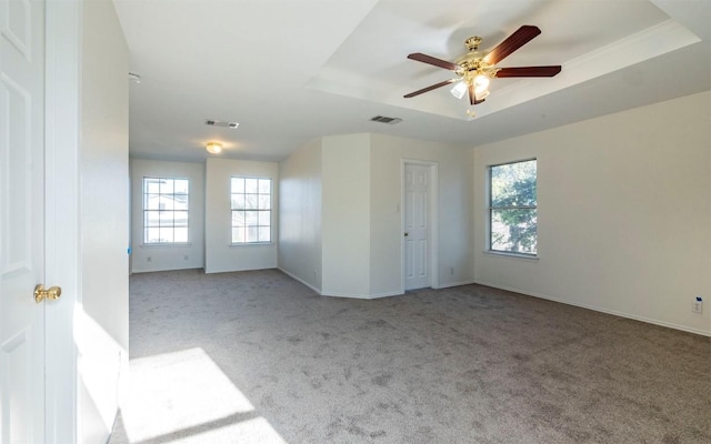 carpeted spare room featuring a tray ceiling, ceiling fan, and plenty of natural light