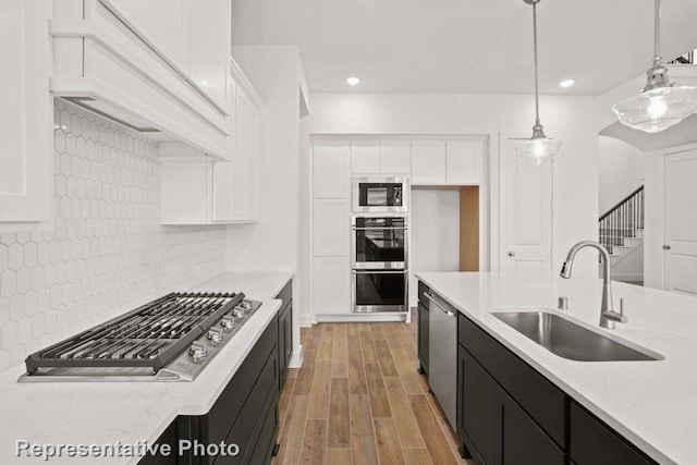 kitchen featuring sink, backsplash, light hardwood / wood-style floors, decorative light fixtures, and white cabinets