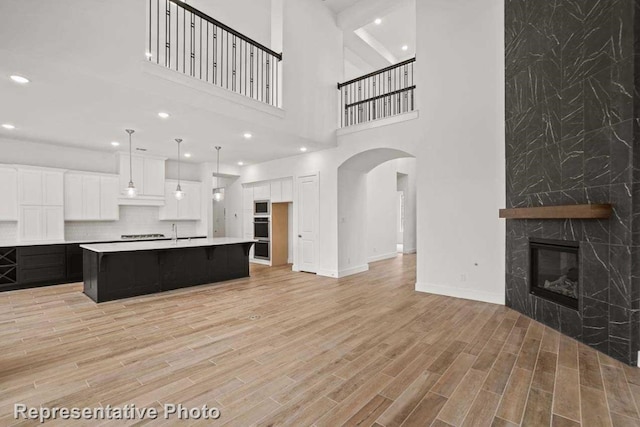 kitchen featuring a center island with sink, a stone fireplace, a towering ceiling, light hardwood / wood-style floors, and white cabinetry