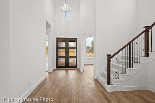 entryway with french doors, a towering ceiling, hardwood / wood-style flooring, and an inviting chandelier