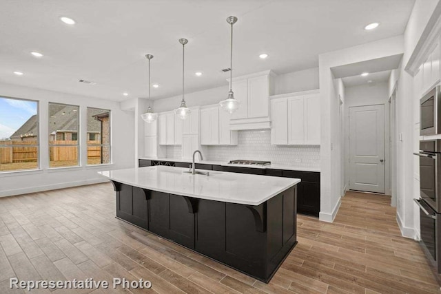 kitchen with white cabinetry, an island with sink, and light hardwood / wood-style floors