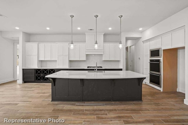 kitchen featuring hanging light fixtures, wood-type flooring, white cabinetry, and a kitchen island with sink