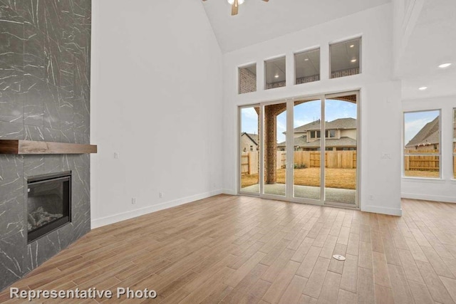 unfurnished living room featuring a high ceiling, light hardwood / wood-style floors, ceiling fan, and a premium fireplace