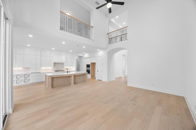 unfurnished living room featuring light wood-type flooring, ceiling fan, baseboards, and arched walkways
