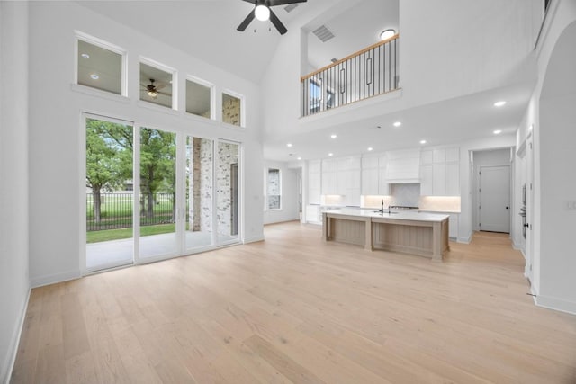unfurnished living room featuring visible vents, baseboards, a sink, ceiling fan, and light wood-type flooring