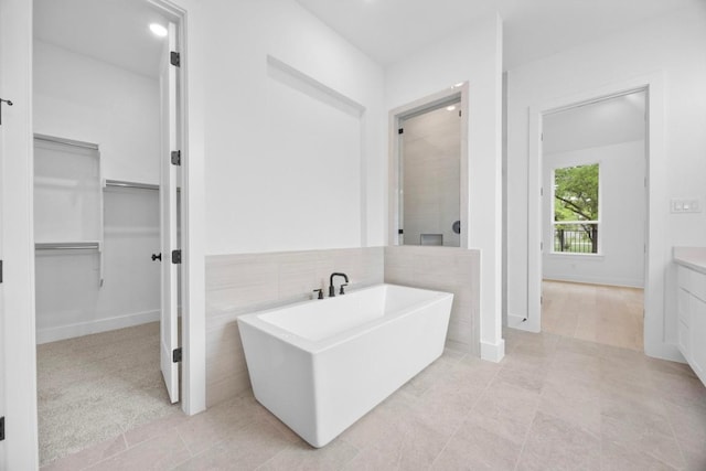 full bath with a tile shower, tile patterned flooring, a spacious closet, and a soaking tub