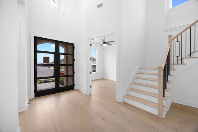 entrance foyer with visible vents, plenty of natural light, a high ceiling, stairway, and wood finished floors
