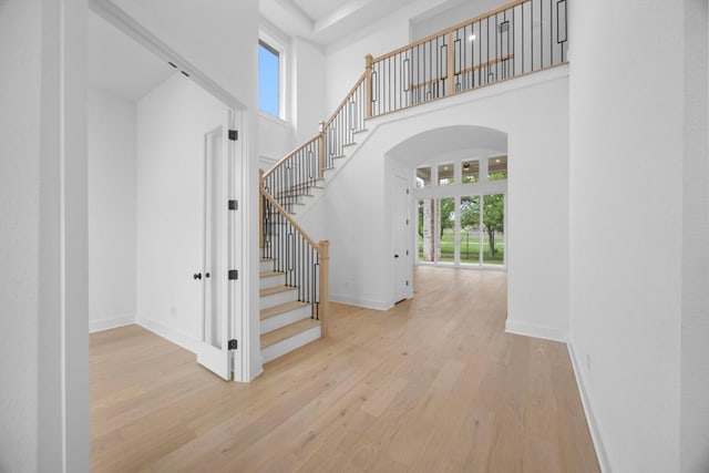 stairway featuring arched walkways, wood finished floors, baseboards, and a healthy amount of sunlight