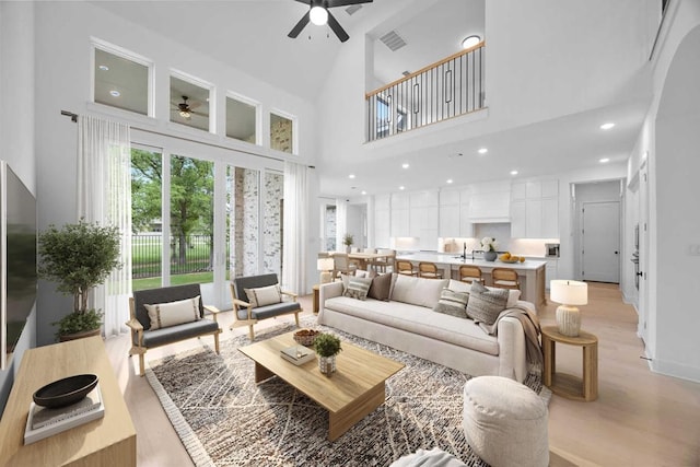 living room featuring light wood finished floors, a high ceiling, ceiling fan, and visible vents