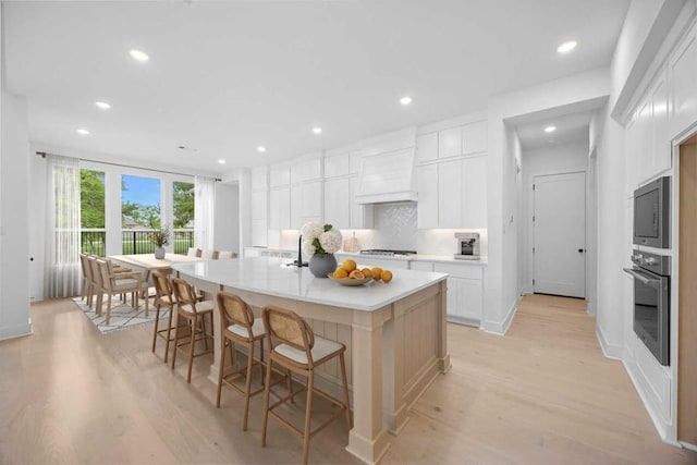 kitchen with custom exhaust hood, backsplash, light wood-type flooring, and appliances with stainless steel finishes