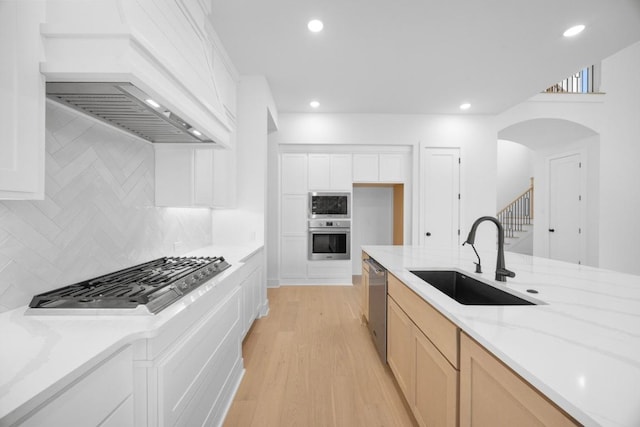 kitchen featuring arched walkways, a sink, appliances with stainless steel finishes, custom range hood, and backsplash