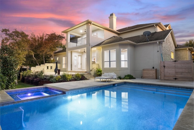 back house at dusk with a swimming pool with hot tub, a balcony, and a patio area