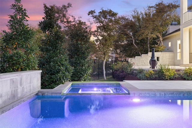 pool at dusk featuring an in ground hot tub