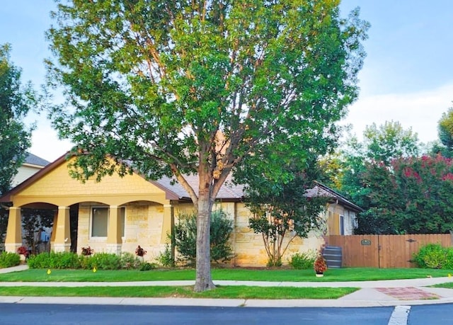 view of front of house with stone siding, fence, and a front yard