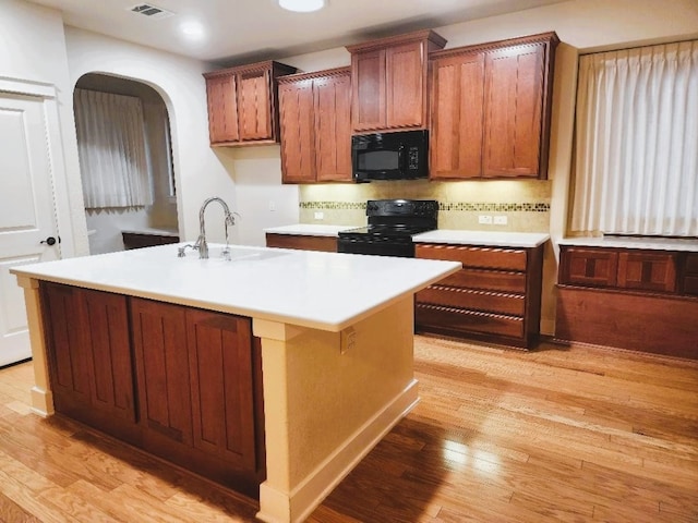 kitchen featuring sink, an island with sink, black appliances, and light hardwood / wood-style flooring