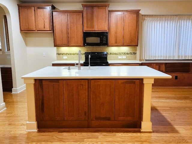 kitchen with a center island with sink, light hardwood / wood-style flooring, and black appliances